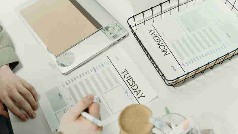 A professional organizing the week with detailed schedule planners in an office setting., tags: auszeiten - pexel